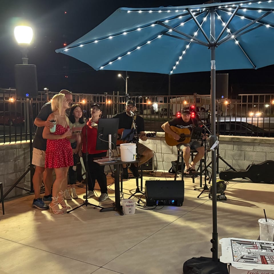 Musicians and guests enjoying live music beneath a lit patio umbrella.